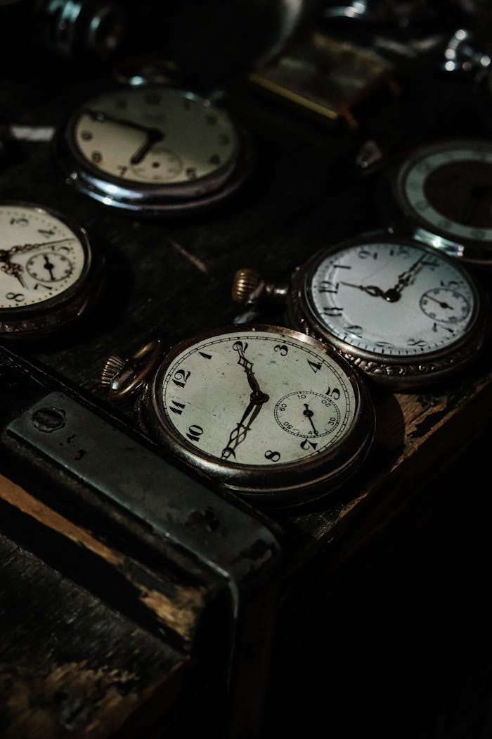A collection of vintage pocket watches displayed on a dark wooden table in low light.